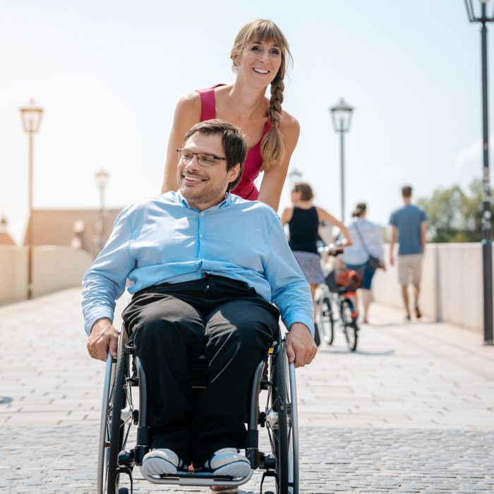 Woman and her friend in a wheelchair having stroll through the town enjoying the sun