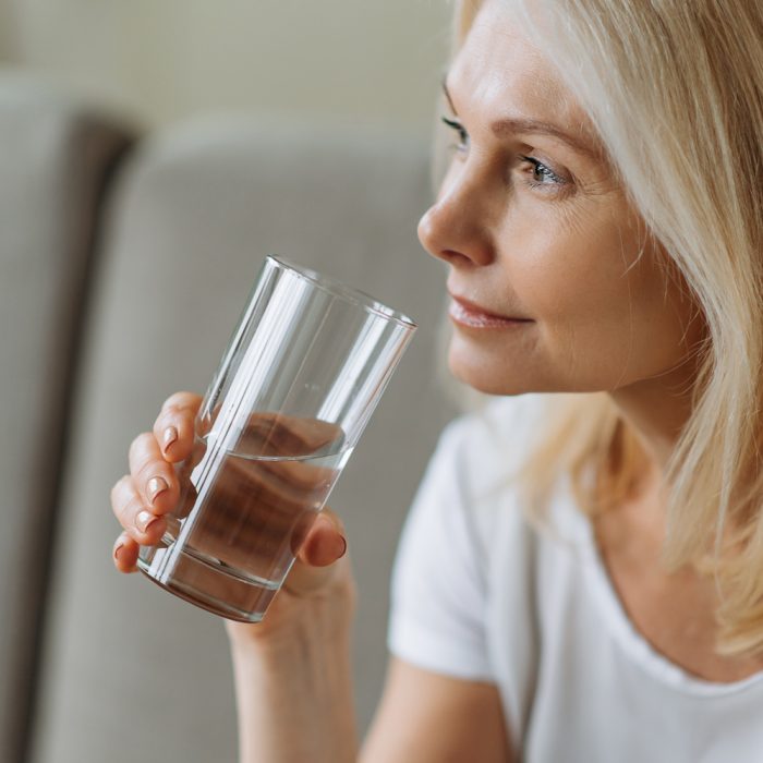 Follow healthy lifestyle. To be healthy. Mature beautiful caucasian woman holding a glass of clean water, taking care of her health, the daily norm of water